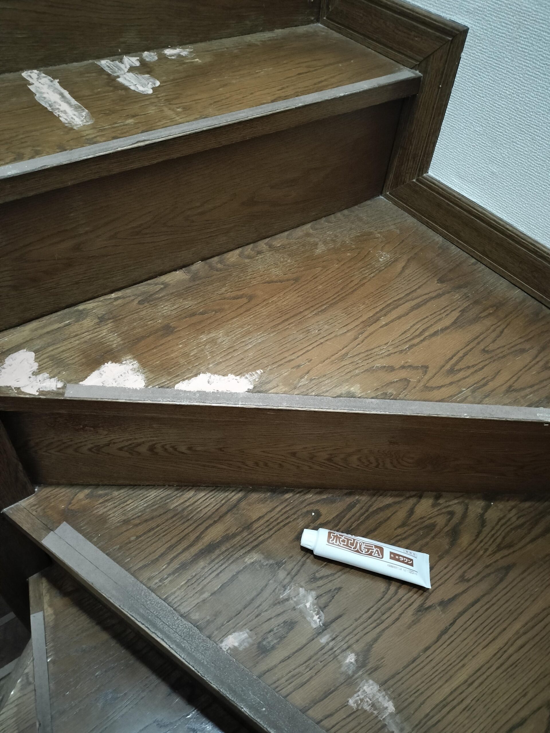 セメダイン木工用パテのチューブと補修中の階段全体。複数箇所に白いパテが塗られている。